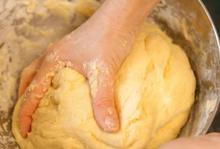 Accorpiamo il latte a filo continuando a lavorare con una frusta mano. Aggiungiamo anche la vanillina e poi passiamo a setacciare la farina e il lievito per dolci. Lavoriamo fino ad ottenere un panetto omogeneo, compatto e appiccicoso;