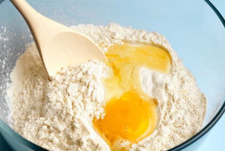 In una ciotola capiente andiamo a riversare la farina, lo zucchero restante, il sale e la scorza di limone; aggiungiamo le uova e iniziamo a mescolare con una forchetta o una frusta a mano;