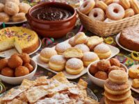 Vassoio abbondante di dolci tipici di Carnevale: chiacchiere croccanti con zucchero a velo, castagnole soffici, sanguinaccio e miglioraccio su tavola addobbata con coriandoli