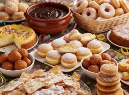 Vassoio abbondante di dolci tipici di Carnevale: chiacchiere croccanti con zucchero a velo, castagnole soffici, sanguinaccio e miglioraccio su tavola addobbata con coriandoli