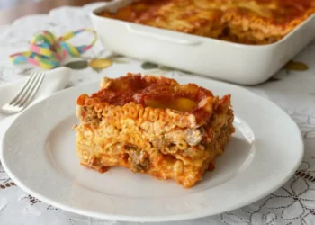 Fetta di lasagna napoletana di carnevale con polpettine e uova sode su tavola imbandita