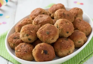 Vassoio di polpette napoletane di Carnevale fritte su canovaccio verde a pois e tavola bianca shabby con stelle filanti.