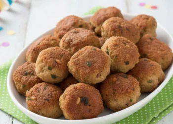 Vassoio di polpette napoletane di Carnevale fritte su canovaccio verde a pois e tavola bianca shabby con stelle filanti.