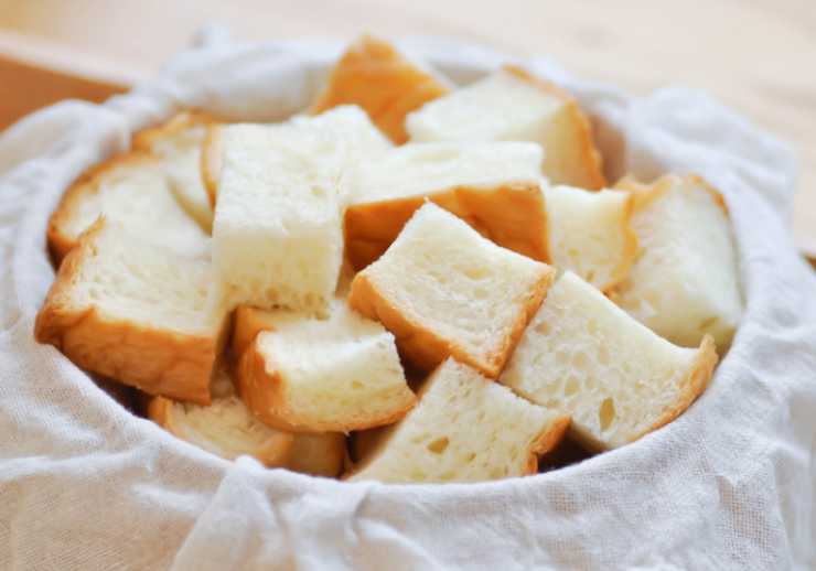 Andiamo a tagliare il pane a fettine e poi ogni fettina a dadini: non importa essere troppo precisi, l’importante è non fare pezzi troppo grandi. Riversiamo in una ciotola e inumidiamo con un filo abbondante di olio d’oliva, rimescolando con cura così da “bagnare” ogni dadino di pane;