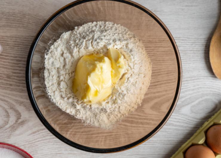 Riversiamo la farina in una ciotola e uniamo il burro a pezzetti. Lavoriamo prima con una forchetta e poi a mano fino a quando non avremo ottenuto un composto sabbioso;