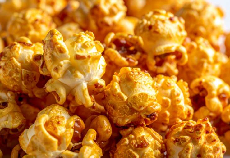 Andiamo a riversare il caramello sui popcorn e mescoliamo velocemente per distribuire su tutti i chicchi prima che asciughi. Se vogliamo evitare che si attacchino andiamo a riversarli in una teglia da forno foderata, distanziandoli e lasciamo raffreddare.