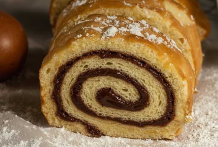 Andiamo quindi a spalmare la crema al cioccolato su di un lato del rettangolo e arrotoliamo aiutandoci con la carta da forno. Sigilliamo i bordi della carta da forno come una caramella e lasciamo assestare per una mezz’ora. Togliamo la carta da forno, sistemiamo in un vassoio e spolveriamo con lo zucchero a velo.