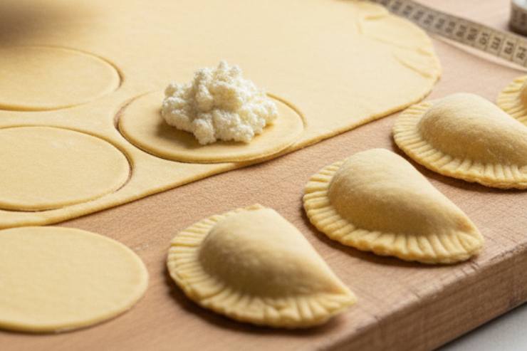 Trascorso il tempo necessario, tirate la pasta sottilissima con il mattarello o la macchina sfogliatrice per la pasta: dovrà essere dello spessore di circa 2 millimetri. Ritagliate dei dischi, farcite con un cucchiaio di crema e chiudete a mezzaluna, sigillate bene i bordi con i rebbi di una forchetta.