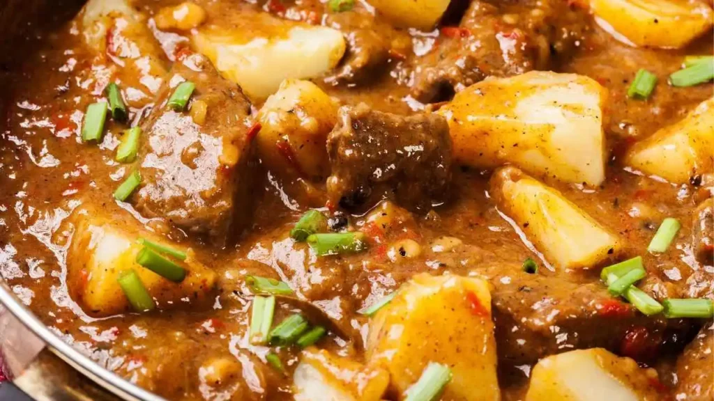 Ciotola bianca di spezzatino con patate tenerissimo fumante, servito su una tavola di legno bianco in una cucina luminosa stile shabby chic con una forchetta su un tovagliolo di lino