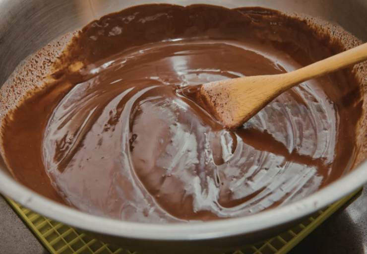 Portiamo il tegame sul fuoco e lasciamo scaldare fino a quando non sfiorerà il bollore. A questo punto uniamo anche il cioccolato fondente tritato e mescoliamo fino a quando sarà del tutto sciolto e amalgamato alla panna e al burro ormai fuso;