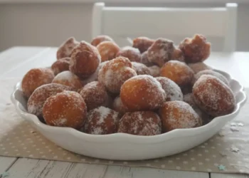 Zeppoline fritte calde appena passate nello zucchero semolato in una ciotola bianca, dorate e soffici.