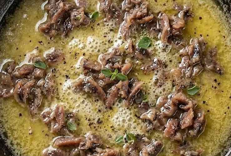Uniamo i filetti di acciughe sott’olio e la scorza grattugiata di un limone al burro e schiacciamo delicatamente finché non si saranno sfaldate formando una sorta di salsa scura. Uniamo un mestolo di acqua di cottura della pasta e mescoliamo per rendere il sugo più cremoso;