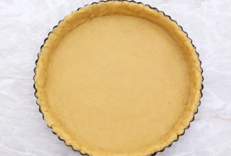 Iniziamo dividendo il panetto di pasta frolla in due porzioni uguali e stendiamole entrambe per ottenere dei dischi della stessa dimensione, quindi sistemiamo il primo in uno stampo per crostate foderato di carta da forno;