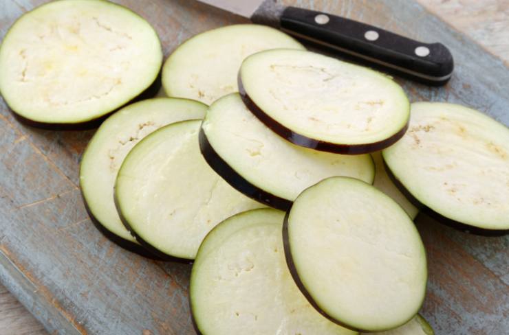 Iniziamo lavando le melanzane, spuntandole e tagliandole a fettine sottili. Intanto, in una padella larga e capiente, riversiamo un giro d’olio e lo spicchio di aglio. Lasciamo dorare e uniamo la passata di pomodoro, copriamo col coperchio e cuociamo a fiamma dolce un quarto d’ora;