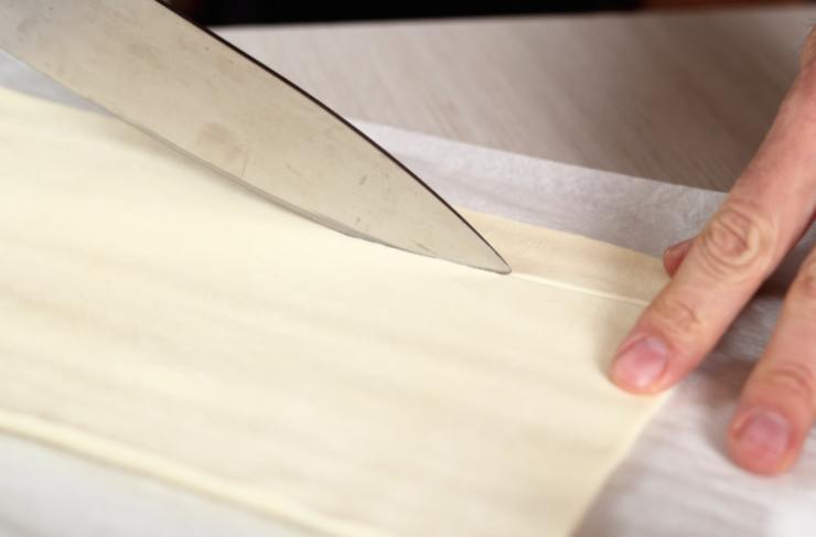 Stendiamo il rotolo di sfoglia su di un ripiano e tagliamo a fettine sottili (un paio di centimetri) nel senso della lunghezza. Dividiamo ogni fettina a metà;