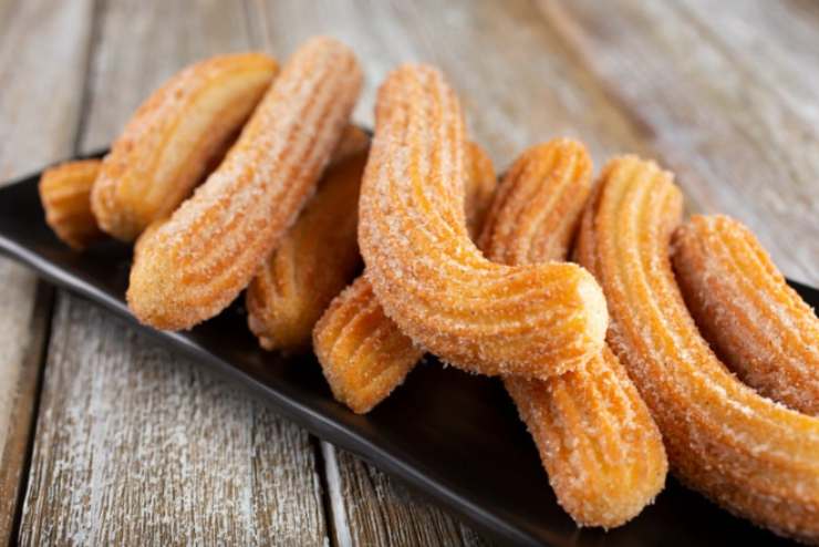 Scaldiamo l’olio di semi in una padella e una volta caldo andiamo a disegnare dei bastoncini con la sac a poche al suo interno, regolandoci con una lunghezza di circa 10 centimetri. Una volta ben dorati i churros sgoccioliamoli dall’olio e rotoliamoli nello zucchero semolato, ricoprendoli completamente.