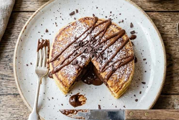 Scaldiamo una padella antiaderente leggermente imburrata e riversiamo al centro un coppino di impasto. Lasciamo cuocere un paio di minuti e adagiamo sopra due o tre pezzetti di cioccolato. Ricopriamo con un altro coppino di impasto e lasciamo dorare qualche altro minuto. Capovolgiamo il pancake e facciamo cuocere anche l’altro lato. Ripetiamo fino a finire l’impasto e una volta impiattati se vogliamo spolveriamo con lo zucchero a velo.