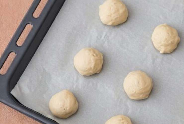 Andiamo adesso a setacciare la farina, la farina di cocco e il lievito, senza mai smettere di mescolare così da evitare la formazione di grumi. Quando saranno assorbiti e avremo ottenuto una sorta di composto semi-denso, prepariamo una teglia da forno foderata. Andiamo a prelevare una porzione di composto con un cucchiaio e lasciamo cadere sulla teglia, cercando di dare una forma rotonda;