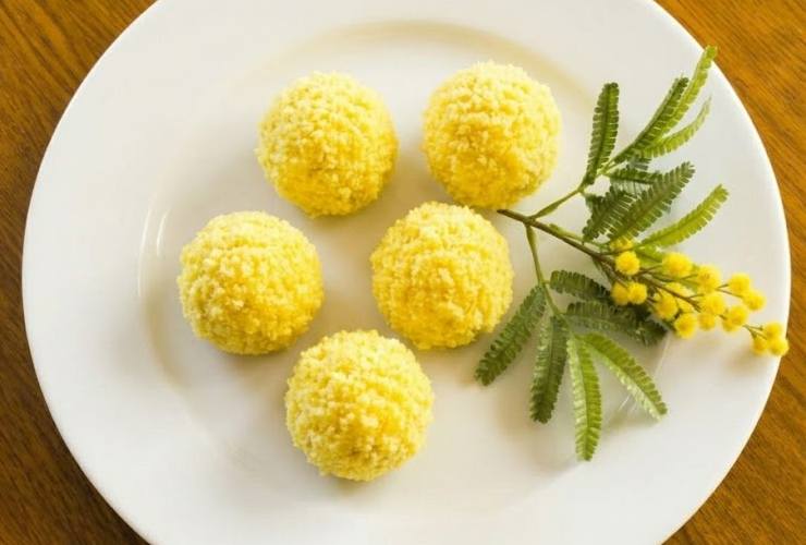 Sciogliamo il resto del cioccolato a bagnomaria e mischiamo le briciole tenute da parte con altra farina di cocco. Immergiamo le palline nel cioccolato bianco fuso e poi rotoliamo in questa sorta di panatura. Lasciamo raffreddare e rassodare il cioccolato ed ecco pronti i nostri tartufini mimosa da servire.