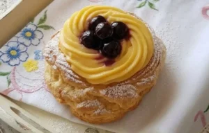Primo piano di una zeppola di San Giuseppe al forno artigianale con crema pasticciera vellutata e amarene sciroppate, consistenza leggera e vuota dentro.