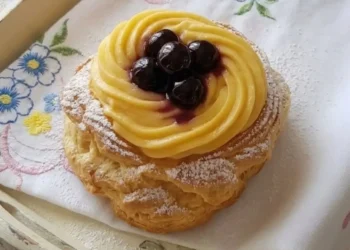 Primo piano di una zeppola di San Giuseppe al forno artigianale con crema pasticciera vellutata e amarene sciroppate, consistenza leggera e vuota dentro.