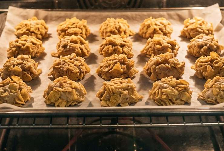 Continuiamo a lavorare fino a ottenere un composto omogeneo e senza grumi, quindi riversiamo all’interno i cornflakes sbriciolati e mescoliamo per distribuire. Preleviamo piccole porzioni di composto e andiamo a rotolarle nei cornflakes per “impanare” assicurandoci di ricoprire ogni lato del biscotto. Ripetiamo fino a finire il composto;