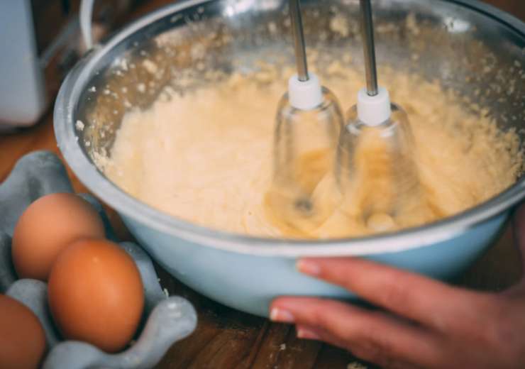 Versiamo il burro fuso nel composto di uova, continuando a mescolare per inglobare. Aggiungiamo lo zafferano, spolverandolo mentre usiamo le fruste delicatamente. Uniamo quindi la farina di nocciole e la farina 00 setacciate, poi l’amido di mais e il lievito, lavorando ancora per evitare la formazione di grumi.
