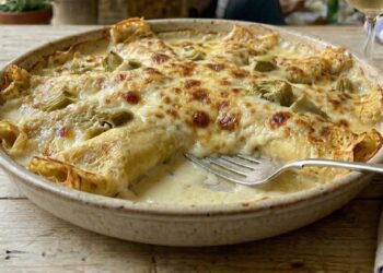 Pirofila rustica con crespelle sottili e dorate ai carciofi, servite con besciamella e gratinate al forno, con ripieno cremoso e carciofi ben visibili.