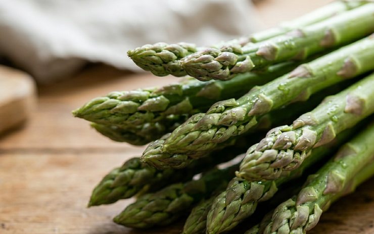 Primo piano delle punte di un mazzo di asparagi verdi freschi con gocce d'acqua.