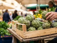 Una cassetta di legno colma di carciofi verdi sferici e turgidi su un banco del mercato all'aperto a Napoli, con sfondo sfocato e soleggiato.