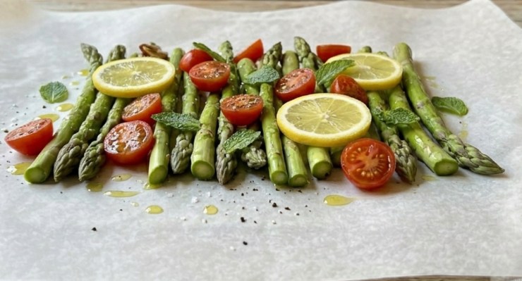 Prendete due fogli di carta forno abbastanza grandi ed adagiate su ognuno un po’ di asparagi puliti (tagliateli a metà se sono troppo lunghi) ed i pomodorini lavati ed asciugati divisi in due. Sciacquate velocemente l’orata pulita ed asciugatela con carta assorbente: inserite nella pancia un pizzico di sale, pepe ed una fetta di limone, quindi appoggiatela sopra le verdure.