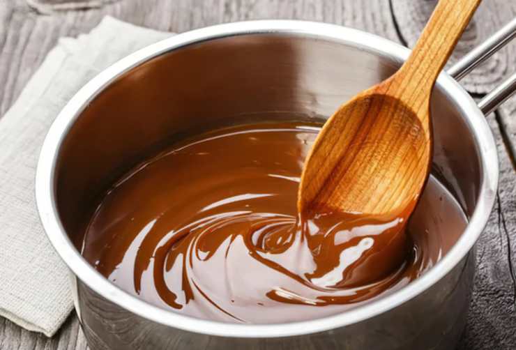 Iniziamo tritando alla meglio il cioccolato e poi sciogliendolo a bagnomaria. Nel frattempo prepariamo una teglia da forno dai bordi alti e foderiamola con la carta da forno;