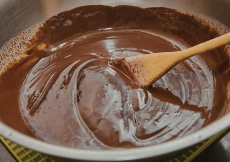 Riversiamo il cioccolato fondente e il burro in un tegame e sciogliamo a bagnomaria. Rimescoliamo e lasciamo raffreddare, quindi accorpiamo il mascarpone e lavoriamo con un frullino per ottenere una crema omogenea;
