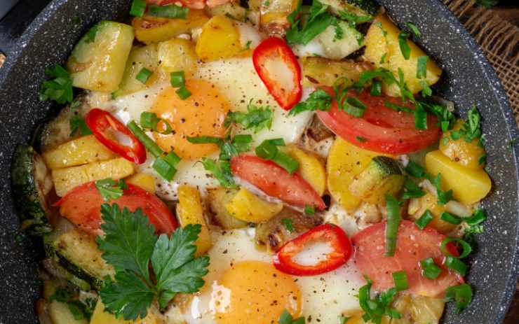 Quando le patate sono quasi cotte, togliamo l’aglio e i pomodori lavati e tagliati a fettine. Facciamo cuocere altri 10 minuti rimescolando spesso. A questo punto creiamo quattro piccoli incavi nella padella, tra le patate il sugo e al loro interno lasciamo cadere le uova sgusciate. Copriamo di nuovo con il coperchio e cuociamo a fuoco basso finché gli albumi risultano sodi. Controlliamo sale e pepe e spolveriamo con gli aromi che più ci piacciono.