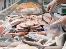 Tranci di pesce spada surgelato sfuso in un banco frigo del supermercato mentre vengono prelevati con una paletta.