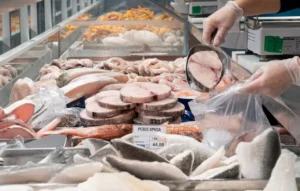 Tranci di pesce spada surgelato sfuso in un banco frigo del supermercato mentre vengono prelevati con una paletta.