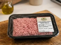 Una vaschetta di carne macinata fresca di bovino confezionata su un tagliere di legno in cucina.