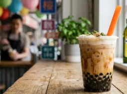 Bubble Tea classico con perle di tapioca Un bicchiere di Bubble Tea classico al latte con striature di sciroppo di zucchero di canna, perle di tapioca sul fondo e una cannuccia arancione, appoggiato su un bancone di legno all'interno di un locale.