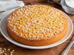 Torta della nonna con crema e pinoli pronta da servire Torta della nonna con pinoli e zucchero a velo servita su piatto bianco rustico.