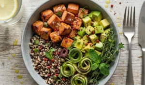 piatti-unici-estivi-light-bowl-quinoa-salmone Bowl di quinoa disposta con cubetti di salmone, avocado a fette e nastri di zucchine alla menta su un tavolo di marmo bianco.