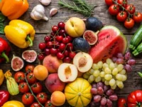 Composizione dall'alto di frutta e verdura estiva di stagione su un tavolo in legno scuro, con anguria, melone, pomodori e peperoni colorati.