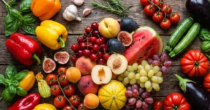 Composizione dall'alto di frutta e verdura estiva di stagione su un tavolo in legno scuro, con anguria, melone, pomodori e peperoni colorati.