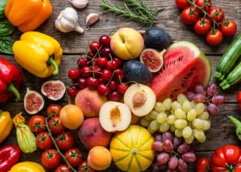 Guida alla scelta della frutta e verdura estiva Composizione dall'alto di frutta e verdura estiva di stagione su un tavolo in legno scuro, con anguria, melone, pomodori e peperoni colorati.