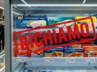 Confezioni di pesce surgelato e surimi nel freezer con cartello di allerta per richiamo lotti contaminati