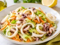Insalata di calamari teneri con sedano croccante, carote julienne, prezzemolo fresco e citronette al limone servita in una ciotola bianca.