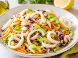 Insalata di calamari teneri con sedano croccante, carote julienne, prezzemolo fresco e citronette al limone servita in una ciotola bianca.