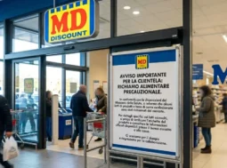 Ingresso di un supermercato MD con un grande cartello informativo in primo piano che segnala un avviso importante di richiamo alimentare precauzionale per la clientela.