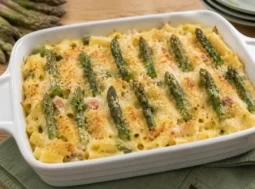 Pasta al forno con asparagi e prosciutto pronta da servire Pasta al forno gratinata con asparagi, prosciutto cotto e besciamella, decorata con punte di asparago e servita direttamente nella teglia dopo la cottura.