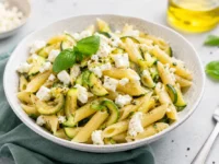 Piatto di pasta fredda con penne, zucchine saltate e feta sbriciolata, ideale per un pranzo estivo leggero e fresco.