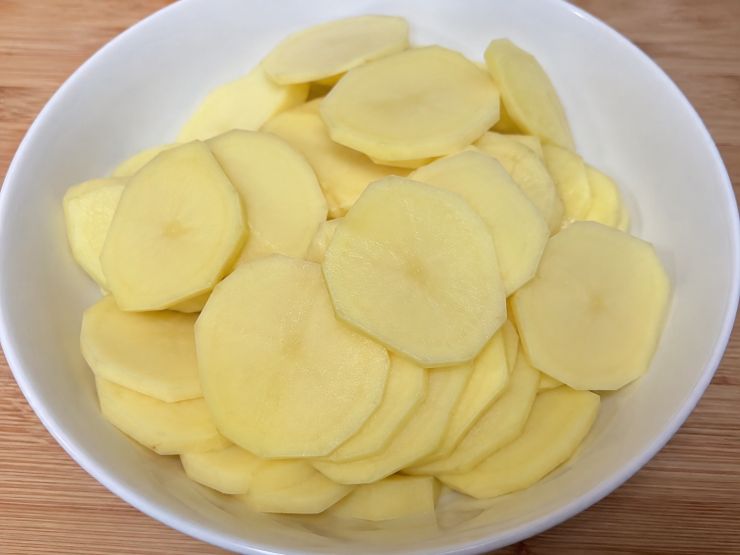 Pelate le patate ed affettatele a rondelle sottilissime, preferibilmente utilizzando una mandolina per ottenere uno spessore uniforme di circa 1-2 millimetri. Immergete immediatamente le fette in una ciotola con acqua ghiacciata per 10 minuti, muovendole spesso per favorire la perdita dell’amido. Scolatele ed asciugatele perfettamente stendendole su un canovaccio pulito.